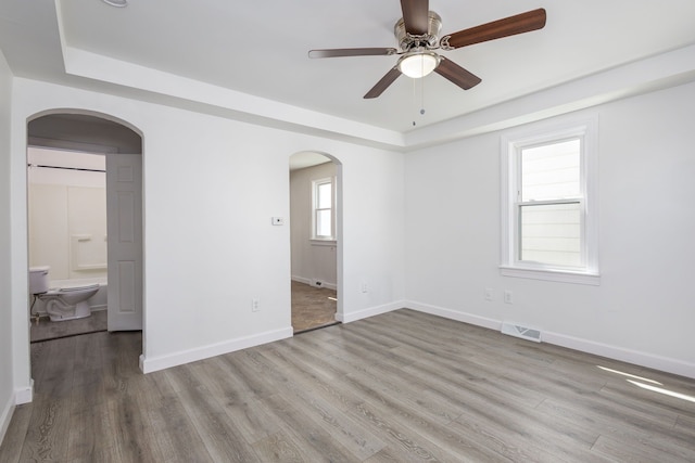 empty room featuring wood finished floors, visible vents, arched walkways, and ceiling fan