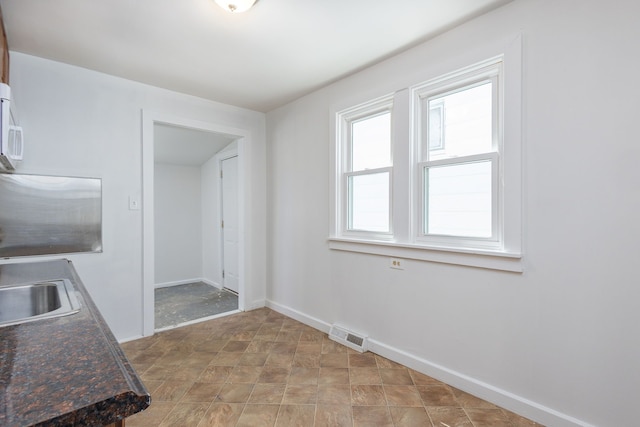 kitchen featuring dark countertops, a sink, baseboards, stone finish floor, and visible vents