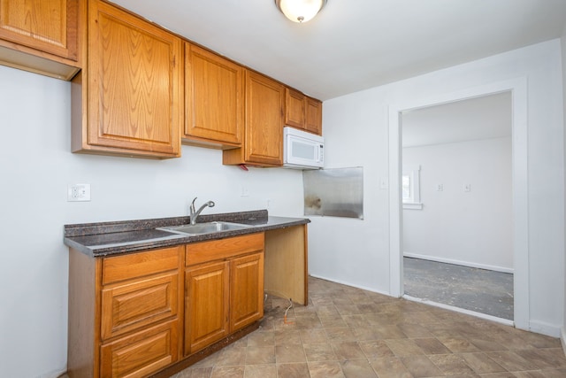 kitchen featuring brown cabinets, dark countertops, white microwave, and a sink
