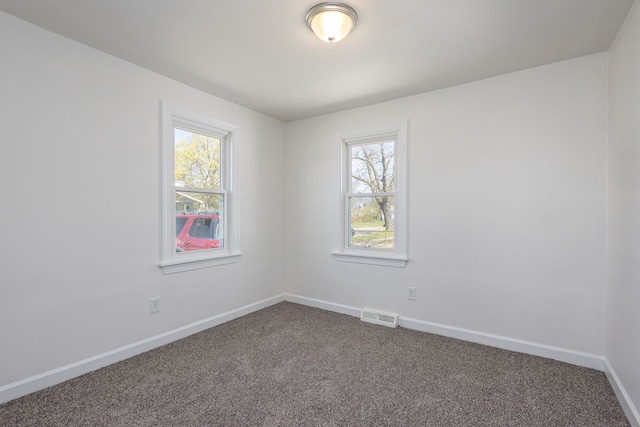 empty room with dark carpet, visible vents, baseboards, and a healthy amount of sunlight