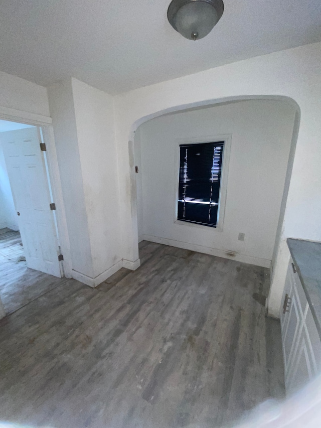 spare room with baseboards, arched walkways, and wood finished floors