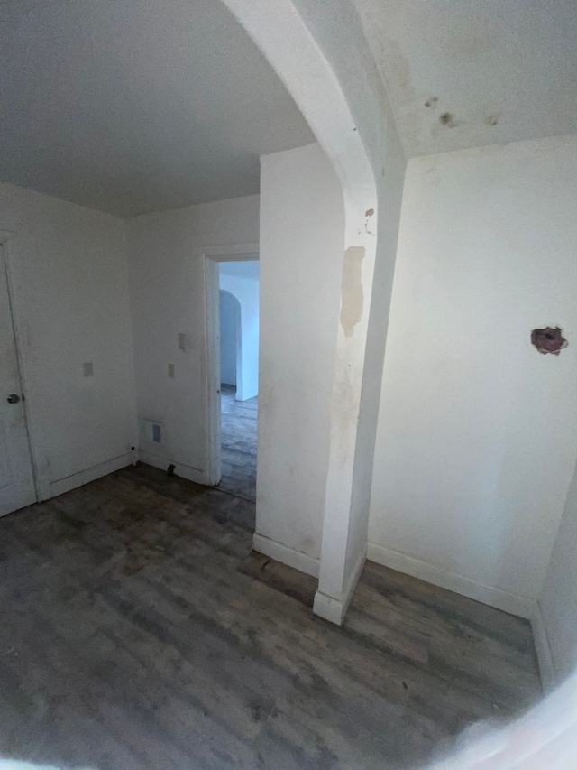 spare room featuring arched walkways, wood finished floors, and baseboards