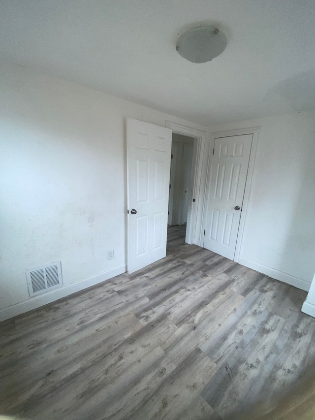 unfurnished bedroom with wood finished floors, baseboards, a closet, and visible vents