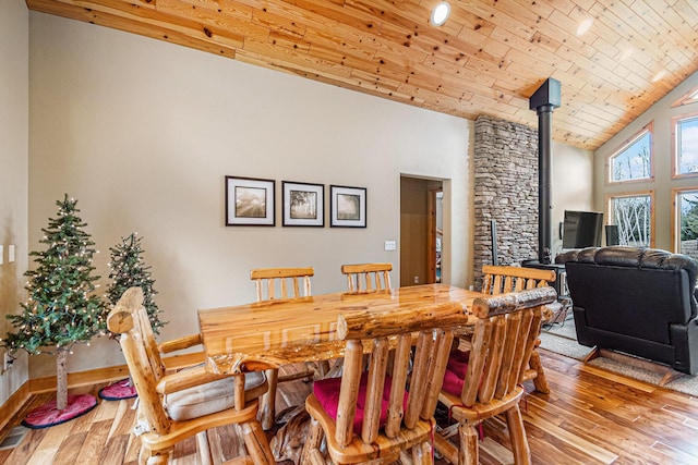 dining space featuring wooden ceiling, a wood stove, wood finished floors, and high vaulted ceiling