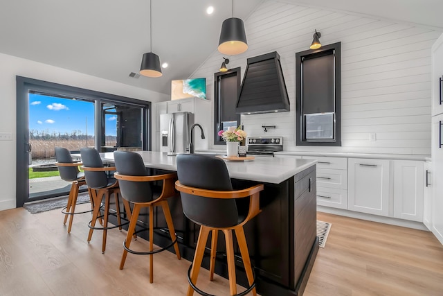 kitchen featuring light countertops, appliances with stainless steel finishes, a center island with sink, custom range hood, and lofted ceiling