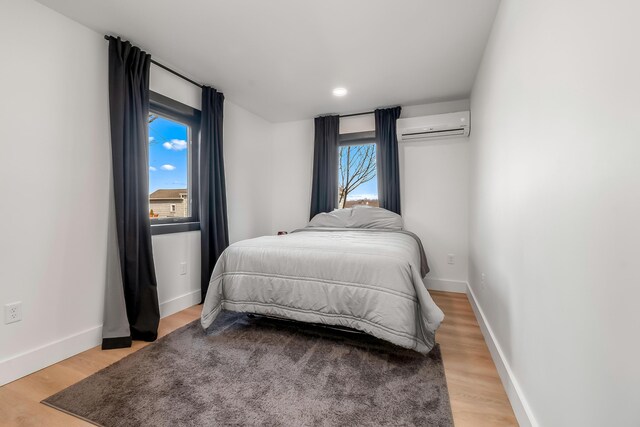 bedroom with a wall mounted AC, multiple windows, and light wood-type flooring