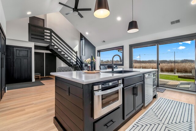 kitchen featuring a sink, light wood finished floors, a center island with sink, and stainless steel appliances