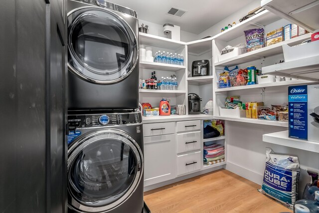 clothes washing area with stacked washer and dryer, visible vents, light wood-type flooring, and cabinet space