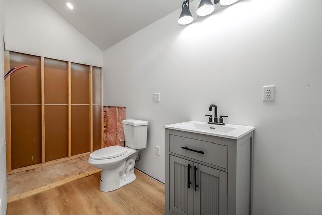 half bath featuring toilet, wood finished floors, vanity, and vaulted ceiling