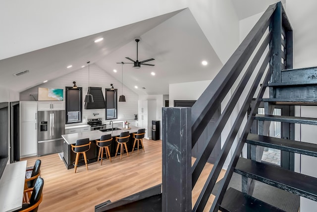 interior space with a breakfast bar, light wood-style flooring, a ceiling fan, stainless steel appliances, and a sink