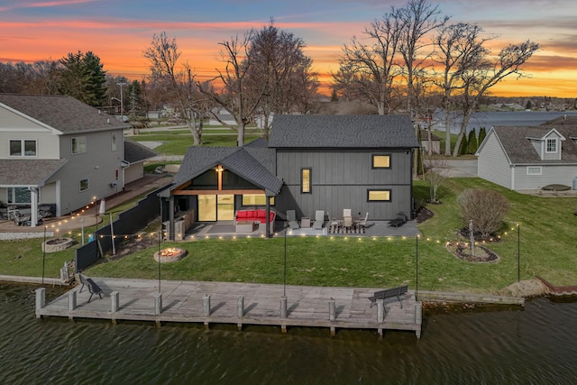 rear view of property featuring roof with shingles, a lawn, a patio, and a water view