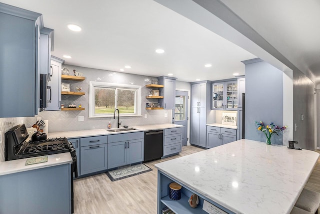 kitchen with black range with gas cooktop, open shelves, dishwasher, a sink, and light wood-style flooring
