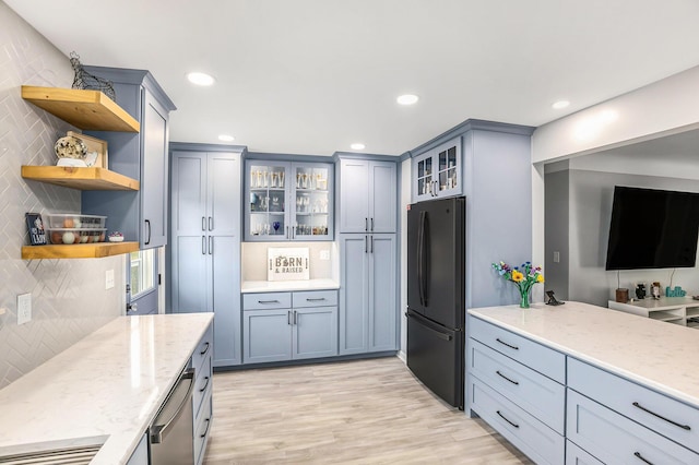 kitchen with dishwasher, freestanding refrigerator, open shelves, and light stone counters