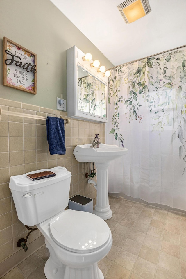bathroom featuring toilet, wainscoting, visible vents, and tile walls