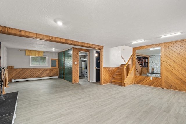 unfurnished living room featuring a baseboard heating unit, wood walls, and wood finished floors