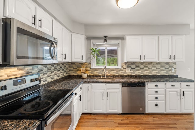 kitchen featuring a sink, white cabinets, dark stone counters, stainless steel appliances, and light wood-style flooring
