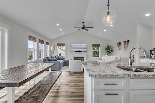 kitchen featuring ceiling fan, white cabinets, a sink, light wood finished floors, and vaulted ceiling