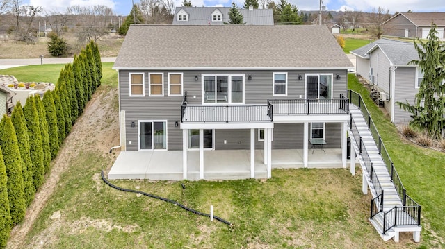back of property featuring roof with shingles, stairs, a wooden deck, a patio area, and a lawn