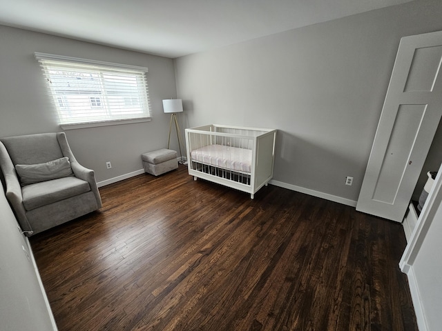 bedroom with baseboards, a crib, and wood finished floors