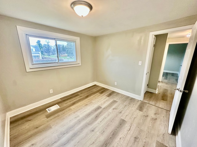 empty room featuring visible vents, light wood-type flooring, and baseboards