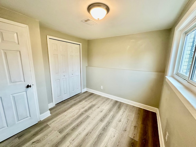 unfurnished bedroom featuring visible vents, baseboards, a closet, and wood finished floors