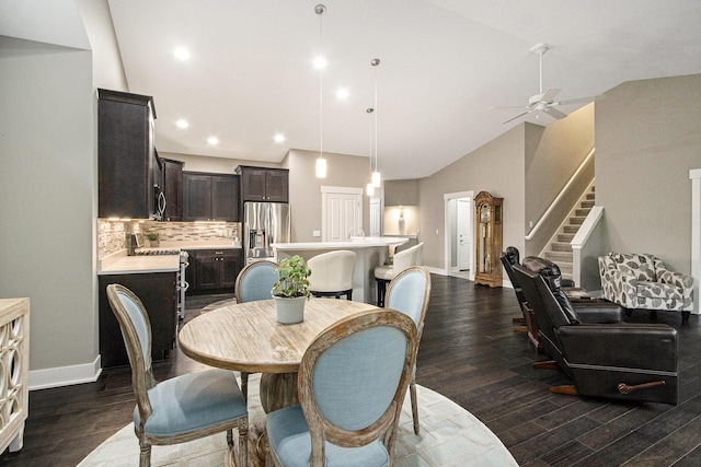 dining area with dark wood-type flooring, high vaulted ceiling, a ceiling fan, and stairs