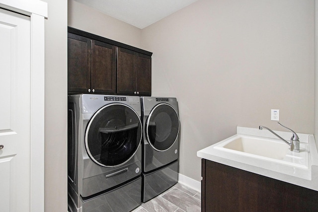 laundry room with baseboards, a sink, cabinet space, and washer and clothes dryer