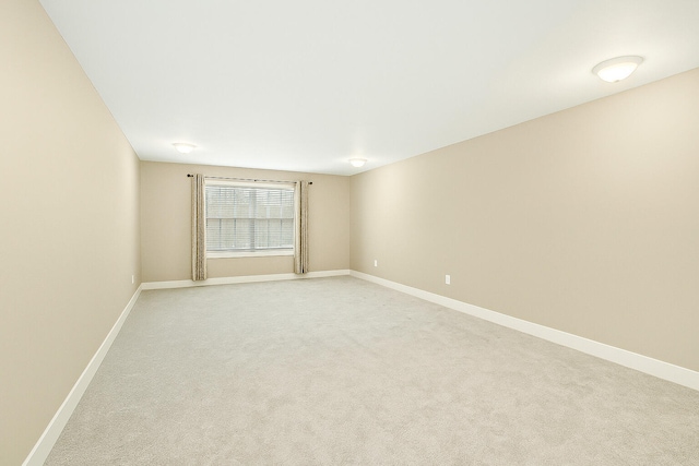 spare room featuring light carpet and baseboards