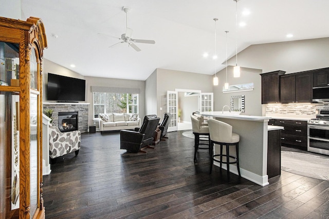 kitchen with a kitchen bar, a ceiling fan, appliances with stainless steel finishes, light countertops, and dark wood-style floors