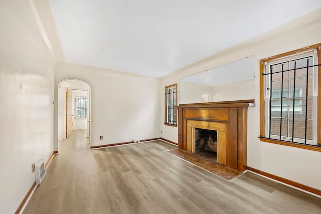 9233 Mckinney St, Detroit, MI 48224 - unfurnished living room featuring a fireplace with flush hearth, arched walkways, wood finished floors, and baseboards