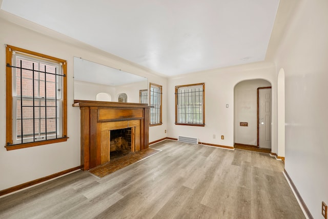 9233 Mckinney St, Detroit, MI 48224 - unfurnished living room featuring a wealth of natural light, a fireplace with flush hearth, arched walkways, visible vents, and wood finished floors