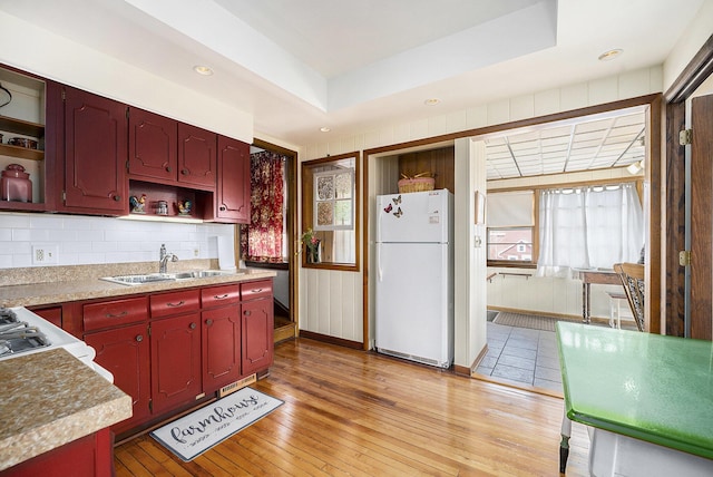 kitchen featuring open shelves, a sink, dark brown cabinets, freestanding refrigerator, and light wood-type flooring