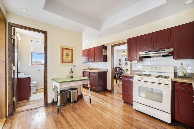 kitchen featuring tasteful backsplash, under cabinet range hood, light countertops, white range with gas cooktop, and light wood-type flooring