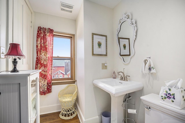 half bathroom with baseboards, visible vents, wood finished floors, and toilet
