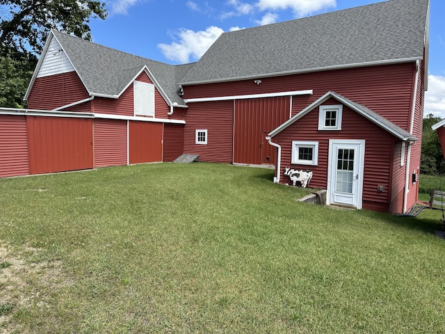 rear view of house featuring a barn, an outbuilding, a yard, and roof with shingles