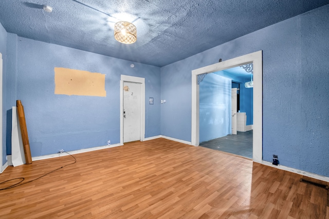 spare room with visible vents, a textured wall, baseboards, and wood finished floors