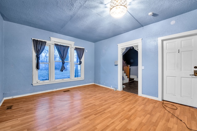 unfurnished bedroom featuring visible vents, a textured ceiling, baseboards, and wood finished floors