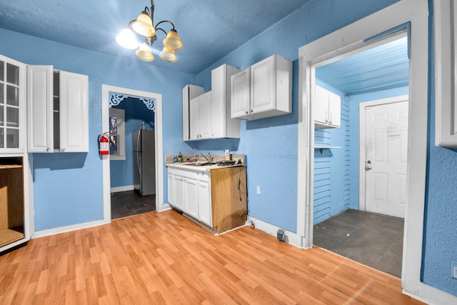 kitchen with a notable chandelier, a sink, light wood-type flooring, freestanding refrigerator, and white cabinetry