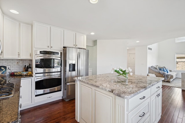 kitchen with light stone counters, a kitchen island, stainless steel appliances, and dark wood finished floors
