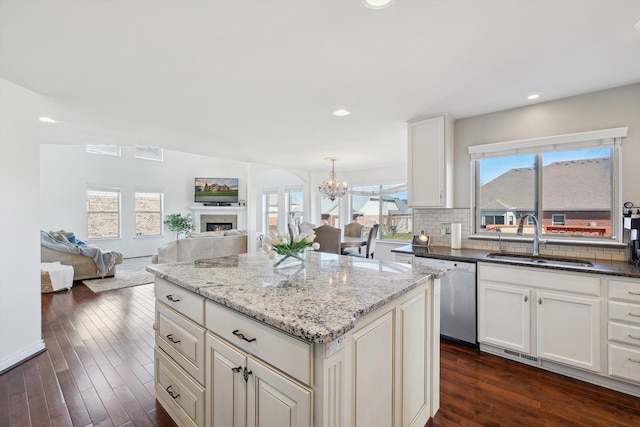 kitchen with light stone countertops, an inviting chandelier, a sink, dishwasher, and a kitchen island