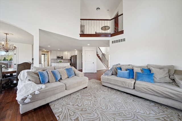 living area with visible vents, wood-type flooring, stairs, an inviting chandelier, and arched walkways