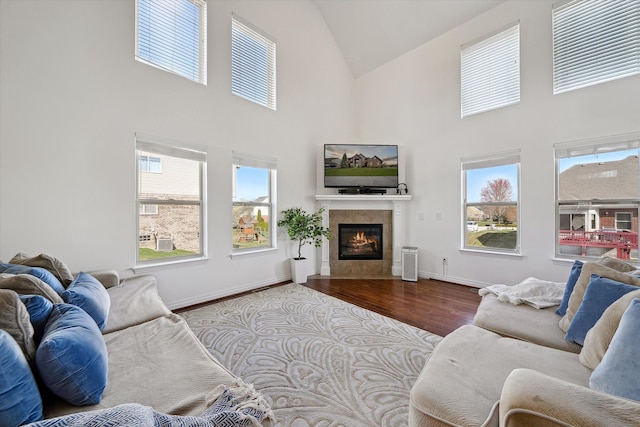 living area featuring baseboards, high vaulted ceiling, a tiled fireplace, and wood finished floors