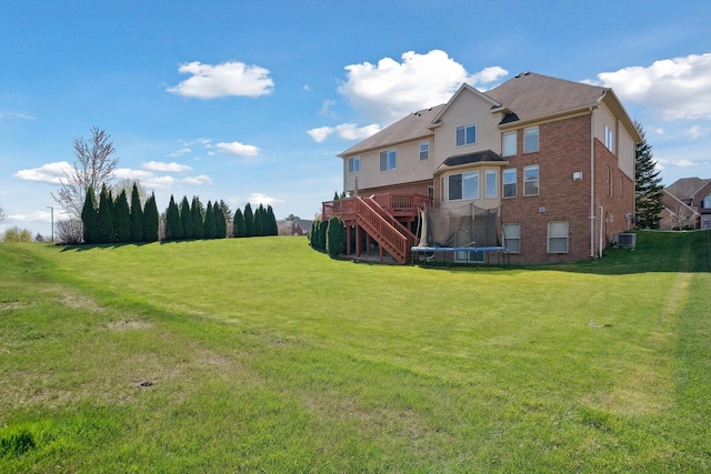 rear view of house with a trampoline, stairs, brick siding, central air condition unit, and a yard