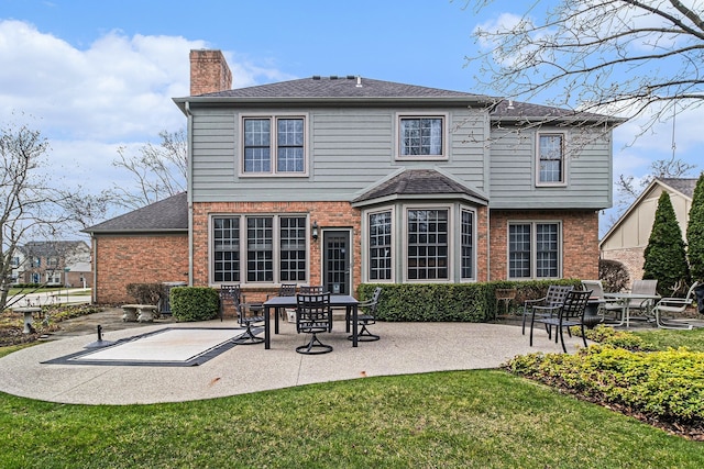 back of house featuring a chimney, a patio area, a shingled roof, a yard, and brick siding