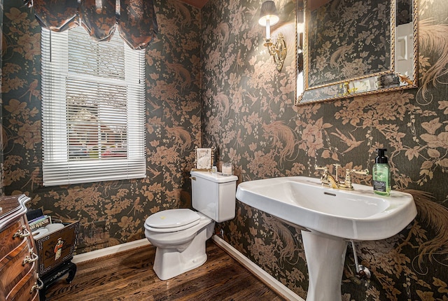half bathroom featuring toilet, wallpapered walls, wood finished floors, and baseboards