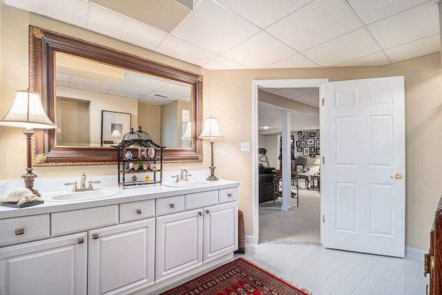 bathroom with double vanity, a sink, and a drop ceiling