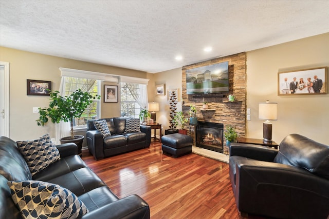 living room with a textured ceiling, a stone fireplace, recessed lighting, and wood finished floors