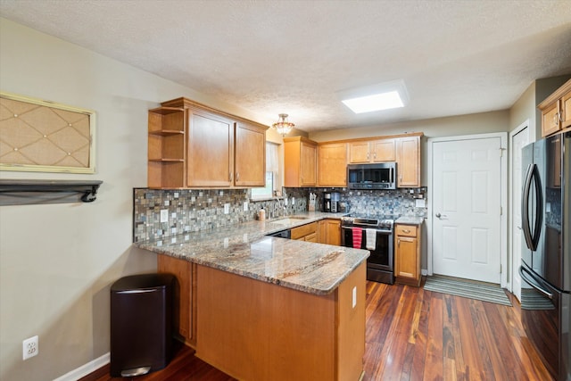 kitchen featuring backsplash, appliances with stainless steel finishes, light stone countertops, dark wood finished floors, and a peninsula