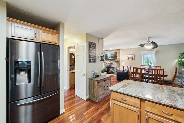 kitchen with light stone counters, stainless steel fridge with ice dispenser, a stone fireplace, open floor plan, and dark wood-style floors