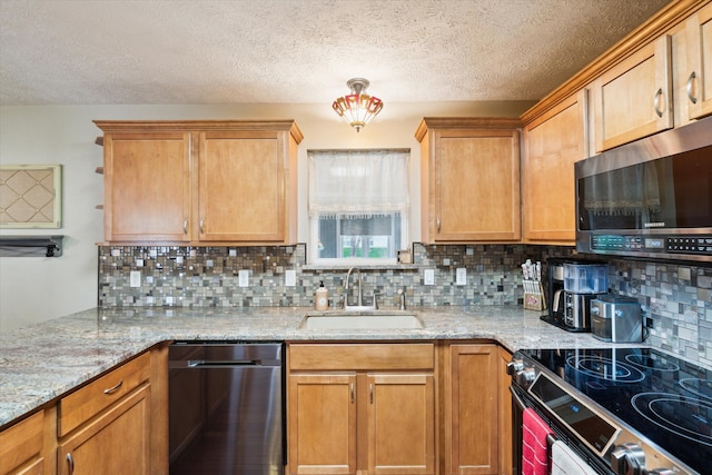 kitchen with light stone countertops, a textured ceiling, tasteful backsplash, a sink, and stainless steel appliances